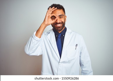 Young Indian Doctor Man Standing Over Isolated White Background Doing Ok Gesture With Hand Smiling, Eye Looking Through Fingers With Happy Face.