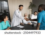 Young Indian doctor wear white coat greeting seminar participant, shaking hand African male intern in blue medical attire start professional medical council meeting in modern conference room. Medicine