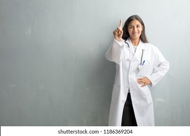 Young indian doctor woman against a wall showing number one, symbol of counting, concept of mathematics, confident and cheerful