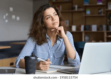 Young indian dreamy thoughtful student looking away working on laptop in office coworking space classroom. Hispanic student using computer for remote learning online training. - Shutterstock ID 1958115754