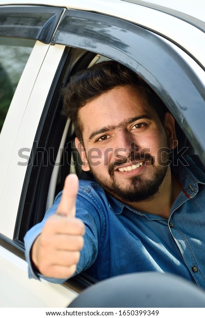 young\
Indian driver showing thumbs up sitting in car\
