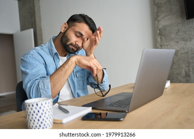 Young indian eastern tired exhausted business man rubbing eyes sitting in modern home office with laptop on desk. Overworked burnout academic Hispanic student with glasses in hand feeling eyestrain. - Shutterstock ID 1979913266