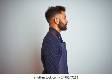 Young Indian Employee Man Wearing Apron Uniform Standing Over Isolated White Background Looking To Side, Relax Profile Pose With Natural Face With Confident Smile.