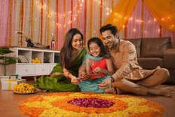 Young Indian Family Making Flower Rangoli For Diwali Festival Celebration. A Healthy Family Sitting Together And Decorating The House, Making Flower Rangoli, Daughter Holding Flower Tray - In...