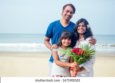 Young Indian Family Relaxing At The Beach On Beautiful Summer Day In Goa With Bouquet Of Roses