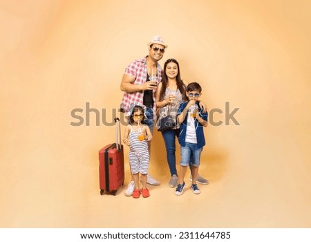 Young Indian family with trolley bag luggage going for summer vacations isolated over beige background, Holidays and travel, copy space,