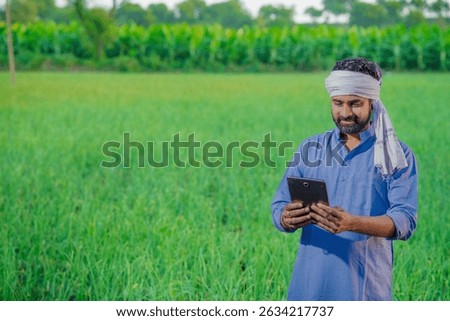 Young indian farmer is using tablet at agriculture field.