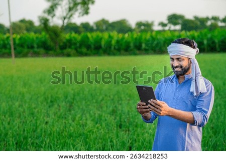 Young indian farmer is using tablet at agriculture field.