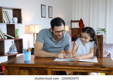 Young Indian father helping charming daughter while studying - education concept. Happy father helping child daughter in studies - sitting together in the living room at home, wearing casual clothes - Powered by Shutterstock