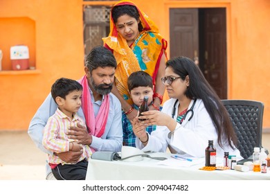 Young Indian Female Doctor with rural family give medicine outdoor village hospital,Healthcare government camp concept. Parents with two son getting medical help and support by pediatrician - Shutterstock ID 2094047482