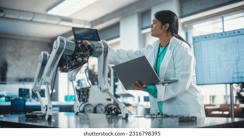 Young Indian Female Engineer Testing Industrial Programmable Robot Animal in a Factory Development Workshop. Professional Researcher in a Lab Coat Developing AI Canine Prototype, Using Laptop Computer - Powered by Shutterstock