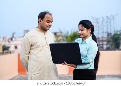 Young Indian Female In Formal Dress With Laptop Showing Something To A Middle Aged Man On Internet, She Is Teaching Computer And Use Of Technology.