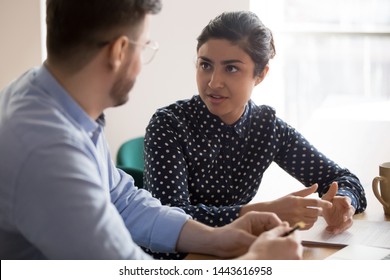 Young indian female mentor coach worker talking to male coworker teaching intern having business conversation with workmate, serious hindu manager helping colleague discussing new project in office - Powered by Shutterstock