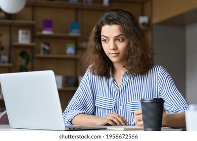 Young Indian Female Student Working On Laptop In Modern Office Coworking Space Classroom. Hispanic Business Woman Using Computer Watching Virtual Online Training Course, Remote Zoom Learning Concept.