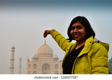 Young Indian Female Tourist Posing In Front Of Taj Mahal. Posing As If Holding The Tip Of Taj By The Tip Of Her Fingers Which A Common Pose And Trick That Visitors Try Here. Agra, Uttar Pradesh, India