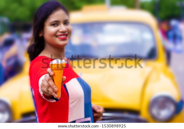 Young Indian girl enjoying ice cream on street\
vendor near taxi stand