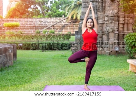 Young indian girl making Vrikshasana Yoga or Tree Pose on yoga mat, exercising outdoor. working out, outdoor close up. Well being, wellness concept