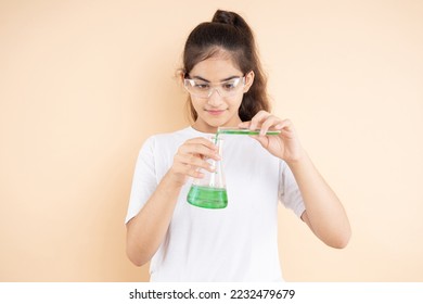 Young indian girl student doing science experiment mixing colorful chemical in a flask isolated over beige background. Education concept. - Powered by Shutterstock