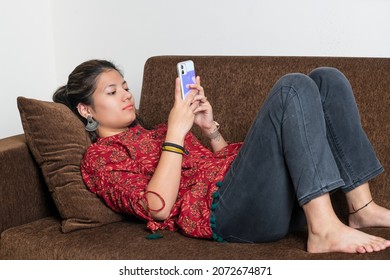 Young indian girl using her mobile phone while lying on the couch. Young generation using mobile phone. Mobile and technology concept.