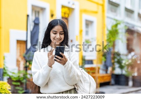 A young Indian girl walks on the city street and uses a mobile phone, calls, waits for an appointment, makes an online payment, rents in booking.