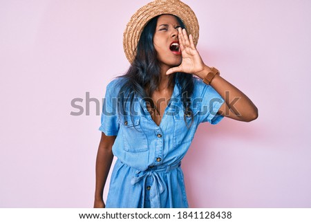 Young indian girl wearing summer hat shouting and screaming loud to side with hand on mouth. communication concept. 