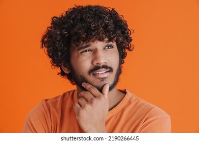 Young Indian Handsome Thoughtful Man Looking Aside Touching His Chin While Standing Over Isolated Orange Background