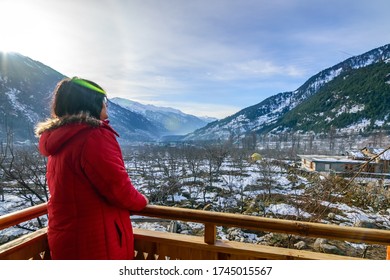 An young Indian lady enjoying the beauty of a snowy Himalayan valley from the balcony 