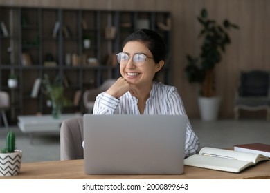 Young indian lady scientist in glasses work on pc do research sit by desk at home in library think of success distracted from screen. Teen female student relax from studying visualize good exam result