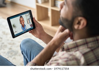 Young Indian Latin Bearded Businessman Having Videocall Meeting At Home With Black Female Doctor Therapist Using Tablet Computer Pointing To Throat. Online Virtual Telemedicine Health Care Concept.