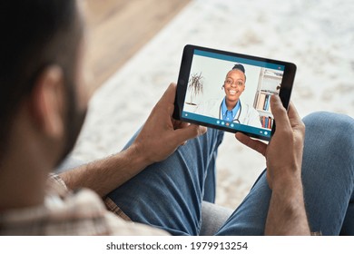 Young Indian Latin Bearded Businessman Having Videocall Videoconference At Home With Black Female Doctor Therapist Using Tablet Computer. Online Virtual Telemedicine Health Care Concept.