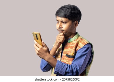 A Young Indian Male In Blue Dress With Thoughtful Face Holding Smart Phone On Gray Background