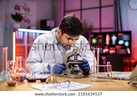 Young indian male researcher looking at the microscope analyze science, forensics, microbiology, biochemistry, genetics, oncology, laboratory.