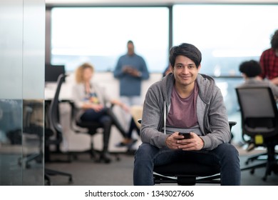 Young Indian Male Software Developer Using Mobile Phone Writing Messages While Having Break At Modern Creative Startup Office