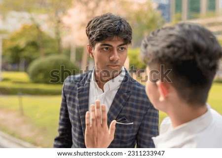 A young indian man bullies and physically threatens his fearful colleague while cornering him at the park. Workplace harassment concept. Stock photo © 