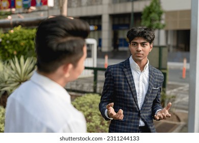 A young indian man debates or explains his opinion to his colleague while outside the office. An animated discussion with hand gestures. - Shutterstock ID 2311244133