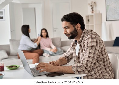 Young Indian Man Father Remote Working Online From Home Office While His Family Wife And Child Daughter Spending Time At Home. Busy Parent Dad Using Laptop Computer Sitting At Table In Homeoffice.