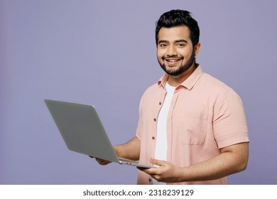 Young IT Indian man he wear pink shirt white t-shirt casual clothes hold use work on laptop pc computer look camera isolated on plain pastel light purple background studio portrait. Lifestyle concept - Shutterstock ID 2318239129