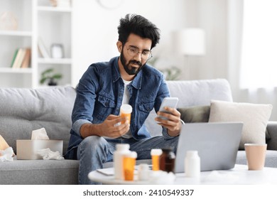 Young indian man holding bottle with pills and using sick eastern male checking doctor prescription in internet, browsing telemedicine app while sitting on couch at home, copy space - Powered by Shutterstock