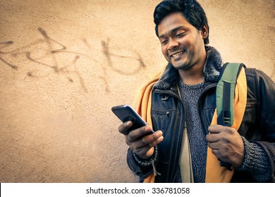 Young indian man holding mobile phone - Cheerful asian model next to old urban wall - Soft vintage filtered look focus on person face 

 

                                                       