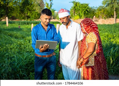 Young Indian Man With Laptop Showing Something To Village Farmer Family On Internet Standing In Green Field, Agriculture Land, Teaching Computer And Use Of Technology. Skill India Concept. 