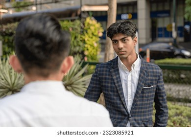 A young indian man listens to a colleague while outside the office. A bit annoyed at his cocky workmates smart aleckness and tall tales. - Shutterstock ID 2323085921