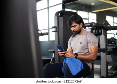 Young indian man monitaring or tracking calories using mobile phone appication at gym - concept of technology, checking workout plans and wellness - Powered by Shutterstock