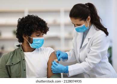 Young indian man in protective face mask got vaccinated against coronavirus at clinic or vaccination site, female doctor or nurse putting adhesive band on shoulder for male patient - Powered by Shutterstock