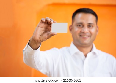 Young Indian Man Showing Blank White Card Mockup Against Orange Background,Smiling Asian Guy Holding Empty Business Or Electronic Card For Payment, Debit,credit, Banking, Selective Focus.