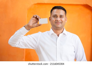 Young Indian Man Showing Blank White Card Mockup Against Orange Background,Smiling Asian Guy Holding Empty Business Or Electronic Card For Payment, Debit,credit, Banking, Selective Focus.