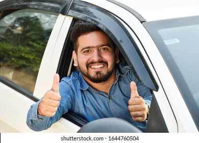 young Indian man showing thumb's up from car, 