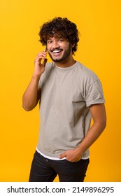 Young Indian Man Talking Phone, Calling To Somebody, Looking At The Camera With Happy Facial Expression. Indoor Studio Shot Isolated On White Background. Vertical Photo