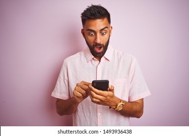 Young Indian Man Using Smartphone Standing Over Isolated Pink Background Scared In Shock With A Surprise Face, Afraid And Excited With Fear Expression