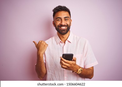 Young Indian Man Using Smartphone Standing Over Isolated Pink Background Pointing And Showing With Thumb Up To The Side With Happy Face Smiling