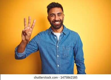 Young indian man wearing denim shirt standing over isolated yellow background showing and pointing up with fingers number three while smiling confident and happy. - Shutterstock ID 1475862185